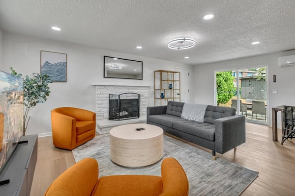 Modern living room with gray sofa, orange accent chairs, round wood coffee table, fireplace, and glass doors to patio