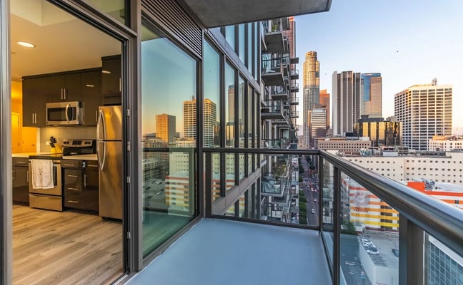 High-rise apartment balcony with city skyline view, modern kitchen with stainless steel appliances visible through glass doors